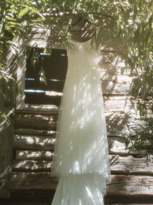 A white wedding dress hanging outdoors with dappled sunlight filtering through leaves.