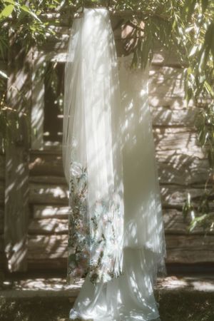 Elegant white wedding dress hanging outdoors with dappled sunlight filtering through leaves creating shadow patterns.