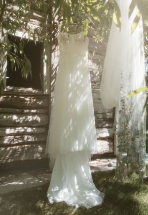 A white wedding dress hangs elegantly in dappled sunlight against a garden backdrop.