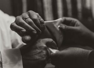 A black and white close-up of hands exchanging rings during a wedding ceremony.