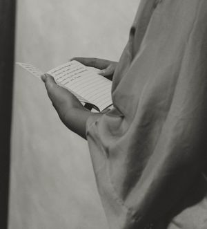 Close-up black and white photograph of hands holding a handwritten letter or note against a light background.