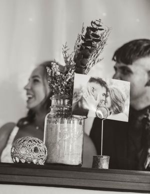 A decorative display featuring a glass jar with flowers and a photo holder on a shelf.