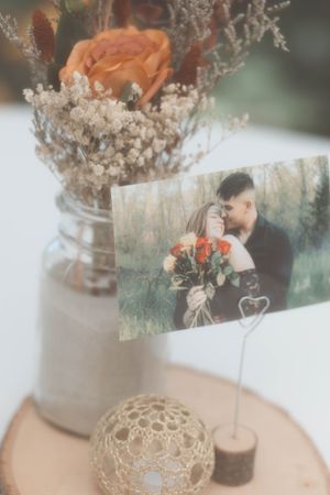 A romantic photograph displayed next to a peach rose in a vase with dried baby's breath and decorative lace orb below.