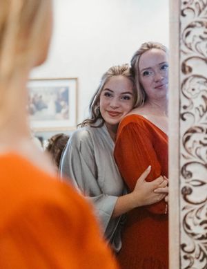 Two friends in casual outfits sharing a joyful moment while looking in an ornate mirror together.