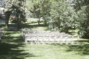 White chairs arranged in rows on a sunlit lawn for an outdoor wedding ceremony.