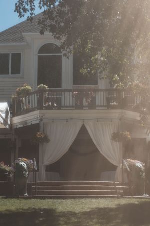 White house exterior with elegant draped curtains and stairs leading to a deck decorated with hanging flower baskets.
