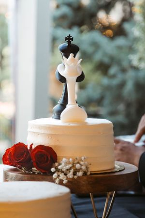 White wedding cake topped with black and white chess piece decorations and red roses.