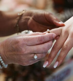 Close-up shot of hands during a wedding ring exchange ceremony with delicate manicured nails.