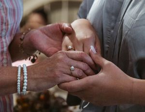 Two hands exchanging rings during a wedding ceremony, with a pearl bracelet visible on one wrist.