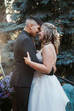 A tender moment between newlyweds embracing outdoors with blue spruce trees in the background.