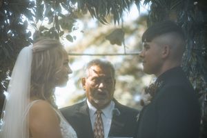 A wedding ceremony takes place outdoors under tree branches with soft lighting.