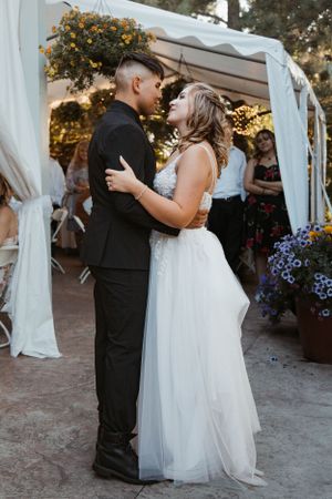 A couple shares their first dance under a white tent decorated with flowers at their wedding reception.