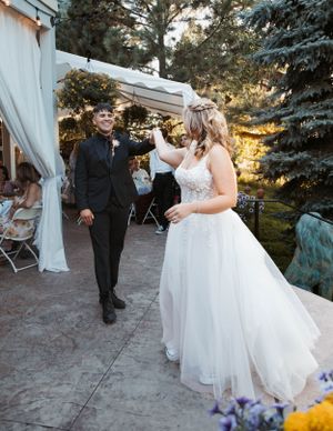 A couple dancing at their outdoor wedding reception with white tent and evergreen trees in view.