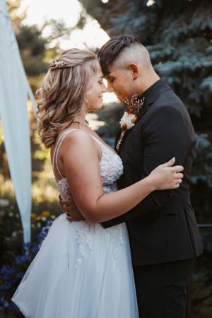 A romantic wedding moment captured at sunset with a bride in a lace gown and groom in black suit embracing outdoors.
