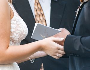 A couple exchanges a small book or document during what appears to be a wedding ceremony.
