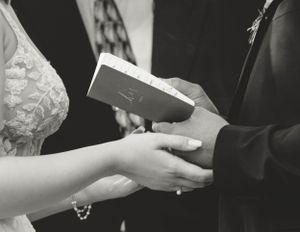 Black and white image of hands exchanging a book during a wedding ceremony.