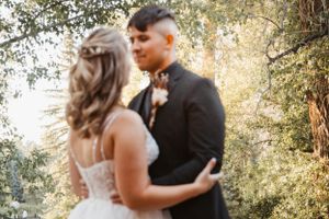 A couple in wedding attire embrace in a romantic outdoor setting with golden sunlight filtering through trees.