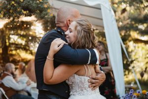A couple shares an intimate embrace during their first dance at an outdoor wedding ceremony at sunset.