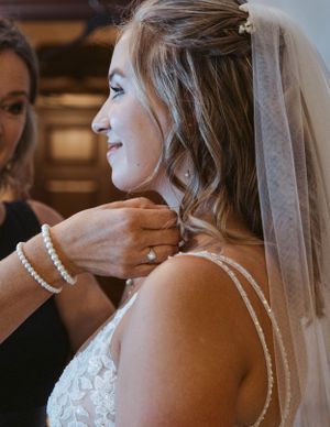 A side view of someone getting jewelry adjusted while wearing a lace wedding dress and veil.