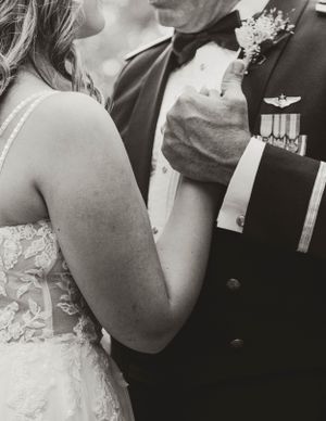 Black and white wedding photo showing a close embrace between a bride in lace and a military service member with medals.