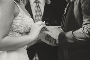 Close-up black and white shot of couple exchanging rings during wedding ceremony.