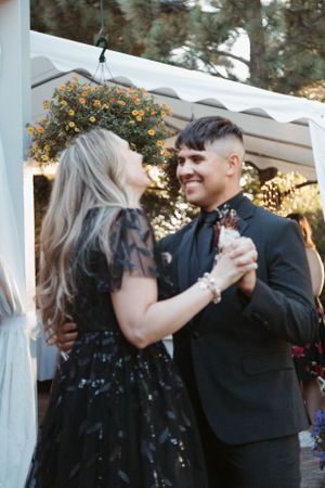 A couple dances together under hanging floral decorations at an outdoor evening celebration.