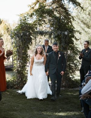 A wedding ceremony under a floral arch in an outdoor garden setting.