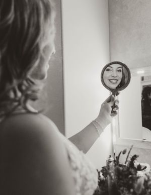 A bride in a white dress looking at her reflection in a handheld mirror.
