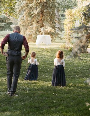 Two young flower girls in navy dresses stand on a grassy lawn with an adult.