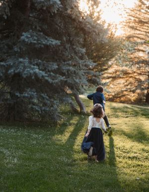 Two children walk through a sunlit garden with evergreen trees at sunset, creating a magical golden hour atmosphere.