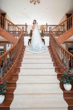 A stunning white wedding dress with blue accents is showcased on an elegant grand staircase with wooden banisters.