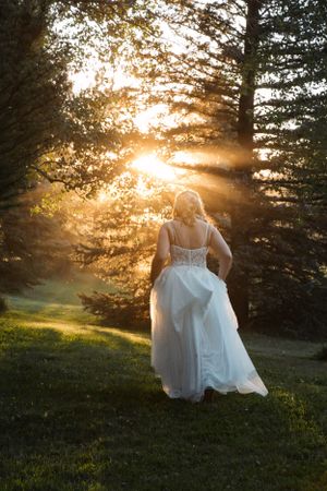A bride in a white dress walking through sunlit trees at golden hour.
