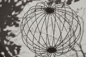 An artistic black and white photograph of a spherical wire sculpture casting intricate shadows.