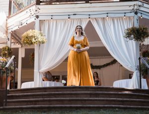 A wedding ceremony setup featuring white drapes and a person in a yellow dress on elevated steps.