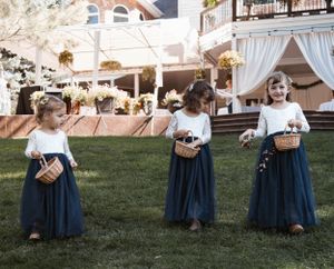 Three children in matching navy blue dresses and white tops stand on a grassy lawn at an outdoor event.