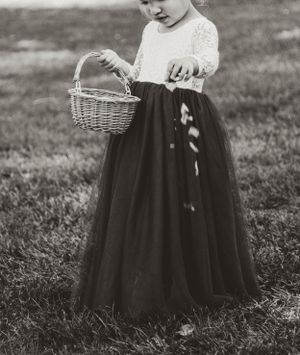 A small child in a black tulle skirt holds a wicker basket in a black and white photograph.