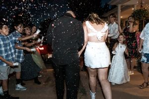 Wedding reception guests dance and celebrate on the dance floor while confetti falls through the air at night.