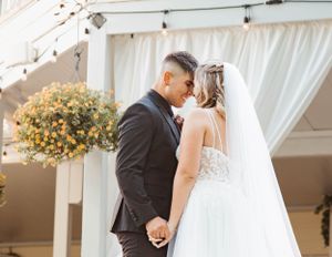 A romantic wedding moment under a white draped canopy with yellow floral arrangements.