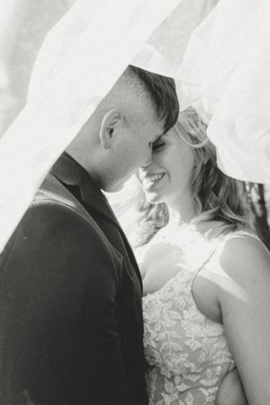 A romantic black and white wedding photo of a couple sharing an intimate moment under a veil.