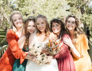 A group in colorful dresses poses together outdoors with dried flower bouquets at a wedding celebration.