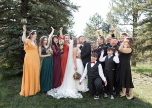 A wedding party poses together outdoors with colorful dresses against a backdrop of pine trees.