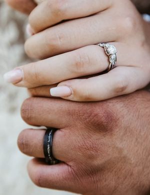Close-up of two hands wearing wedding rings, one with a diamond engagement ring and one with a black band.