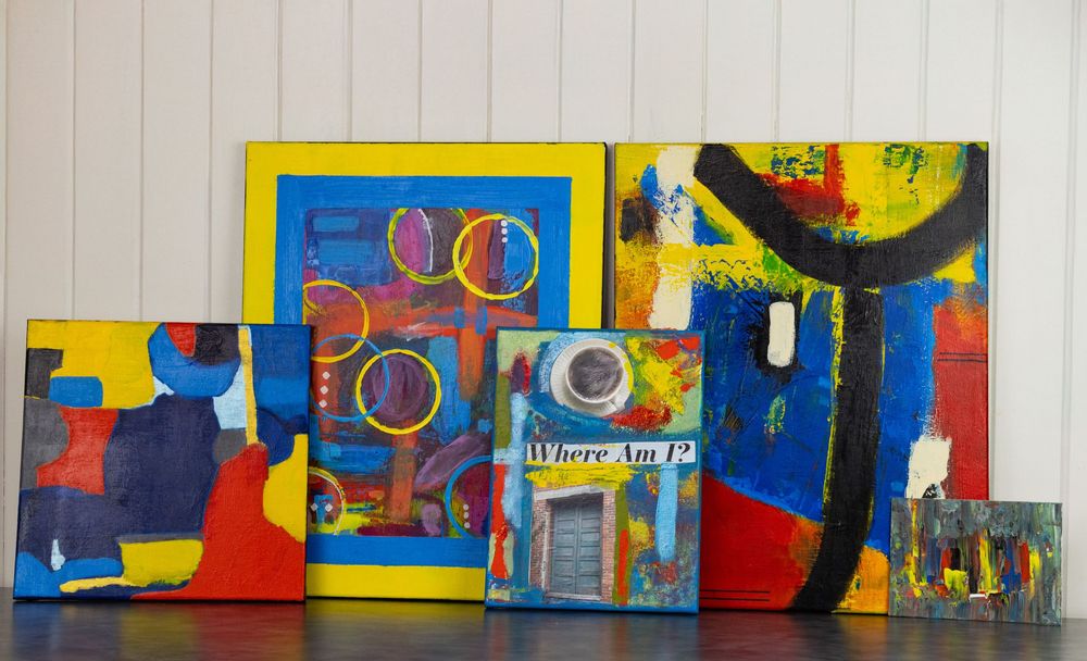 Group of colorful abstract paintings arranged together on a white floor, showcasing bold primary colors and mixed media styles.