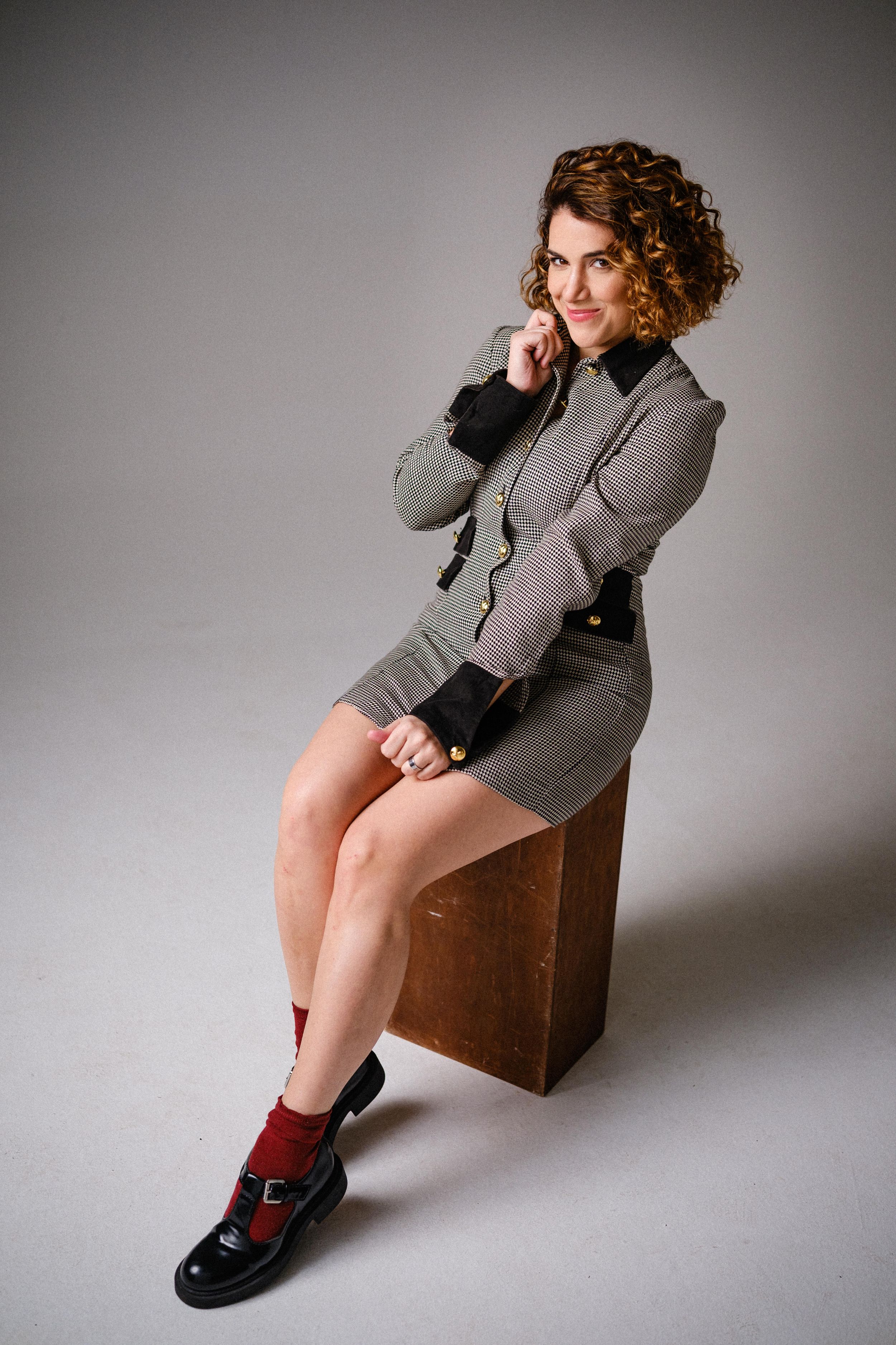 Fashion model in gray houndstooth dress and red socks poses on brown cube.