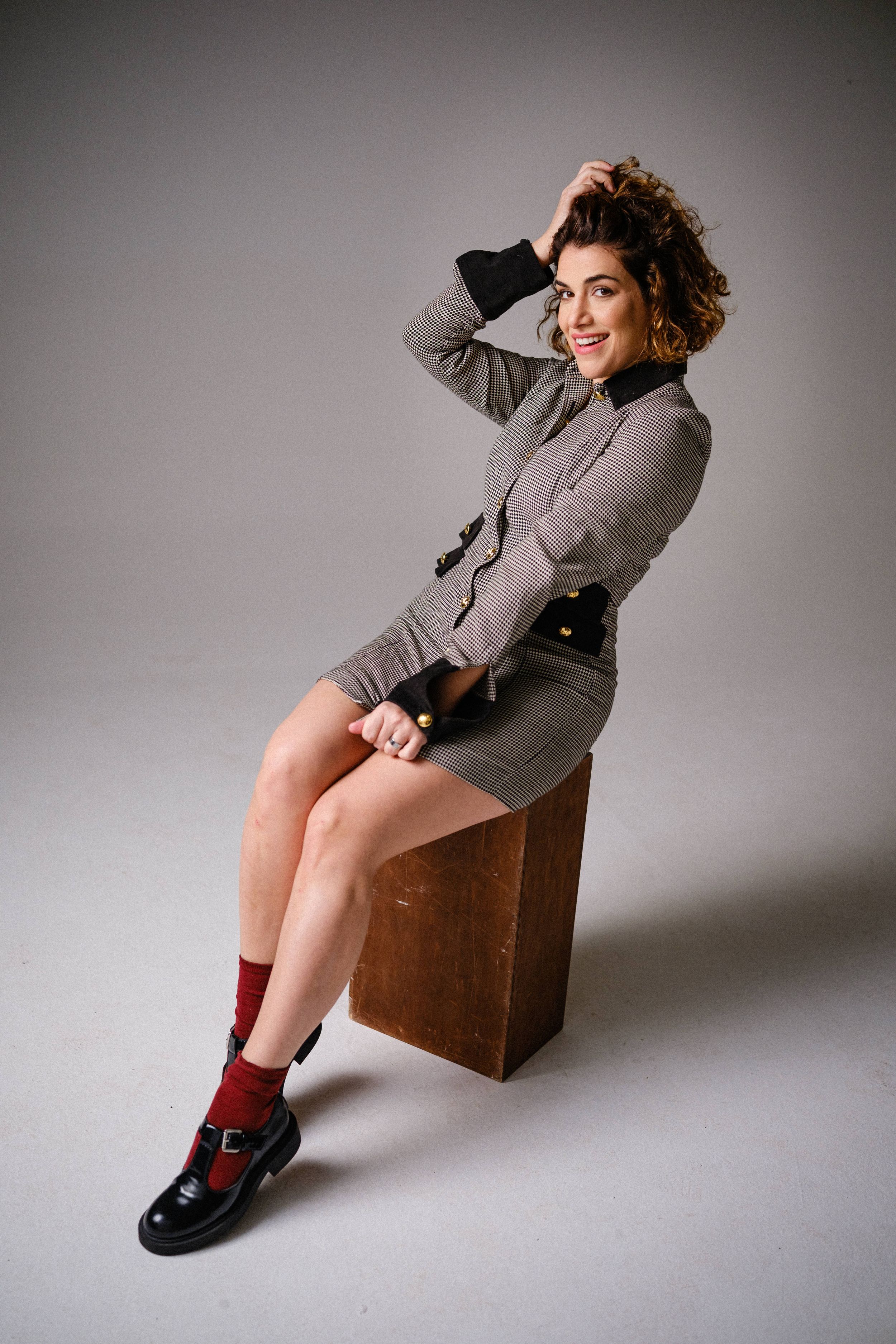 Playful fashion shot of model in houndstooth dress with red socks and black shoes.
