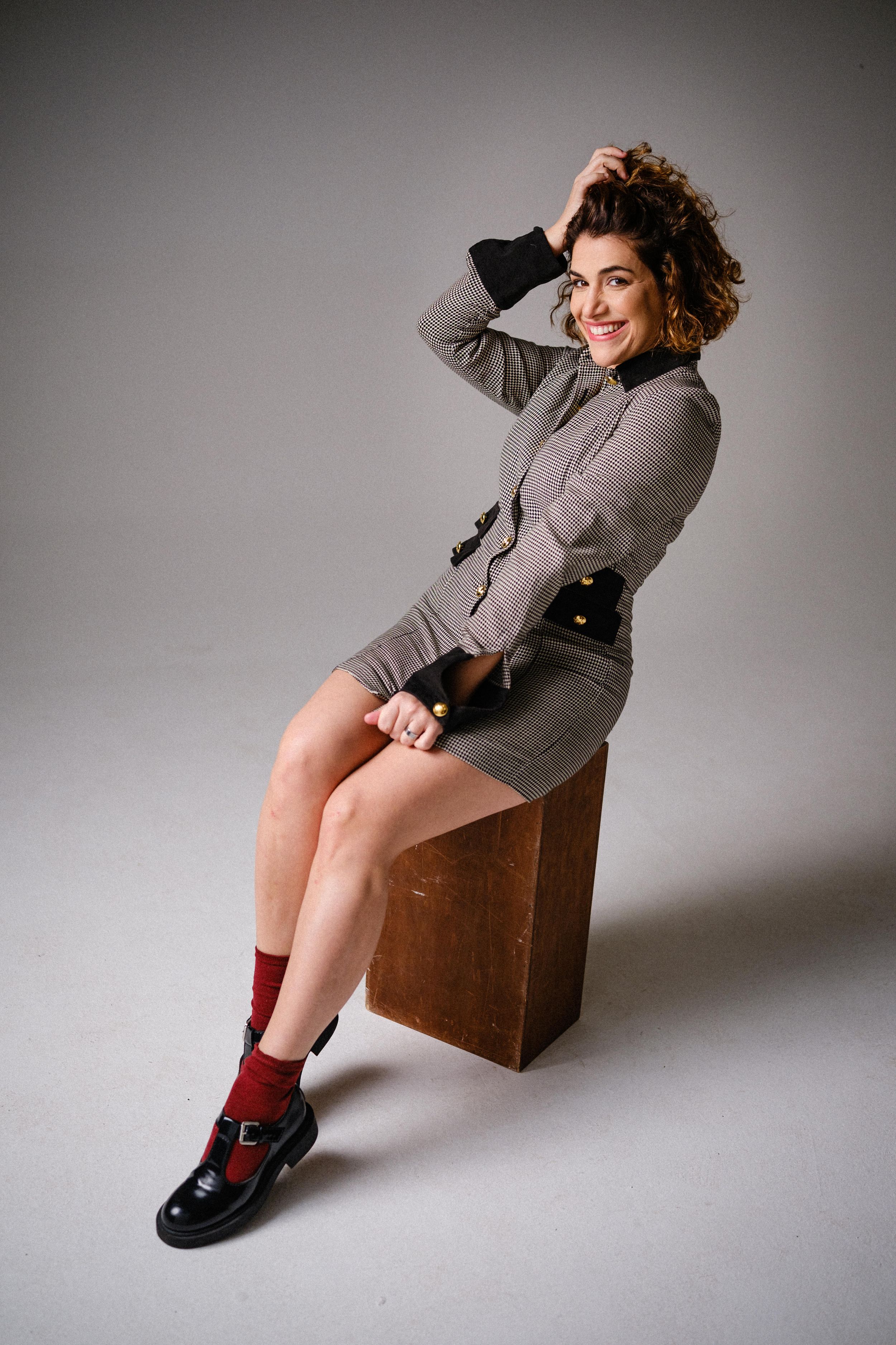 Dynamic pose of model in gray houndstooth dress with red socks on wooden block.