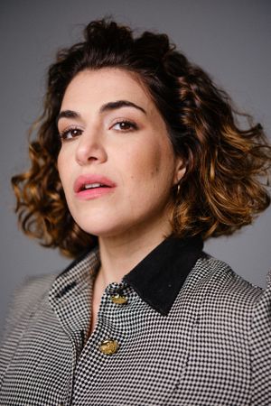 Beauty shot highlighting curled hair and houndstooth jacket with gold button details.