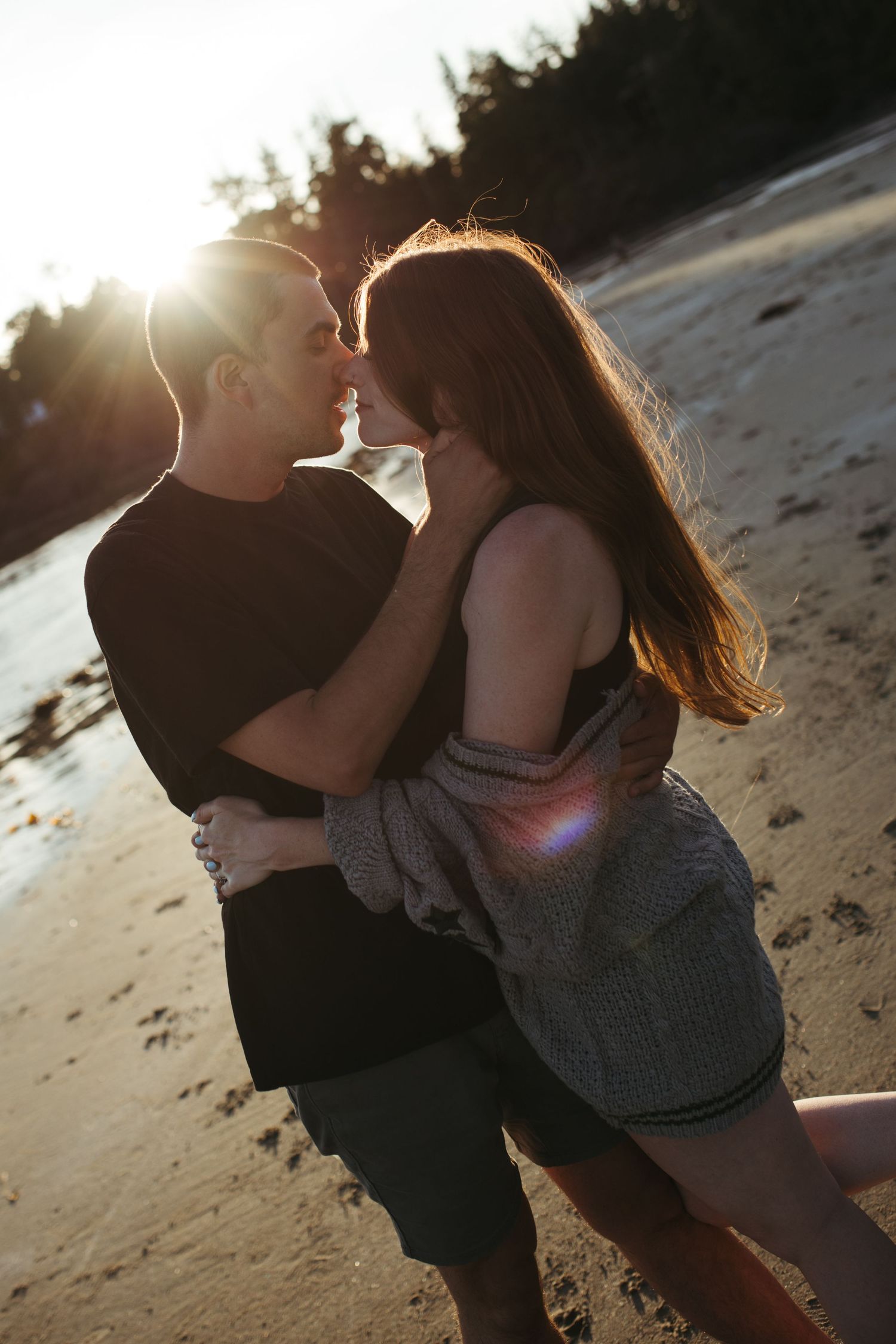 Couple embracing and almost kissing on a sandy beach at sunset with golden backlight.
