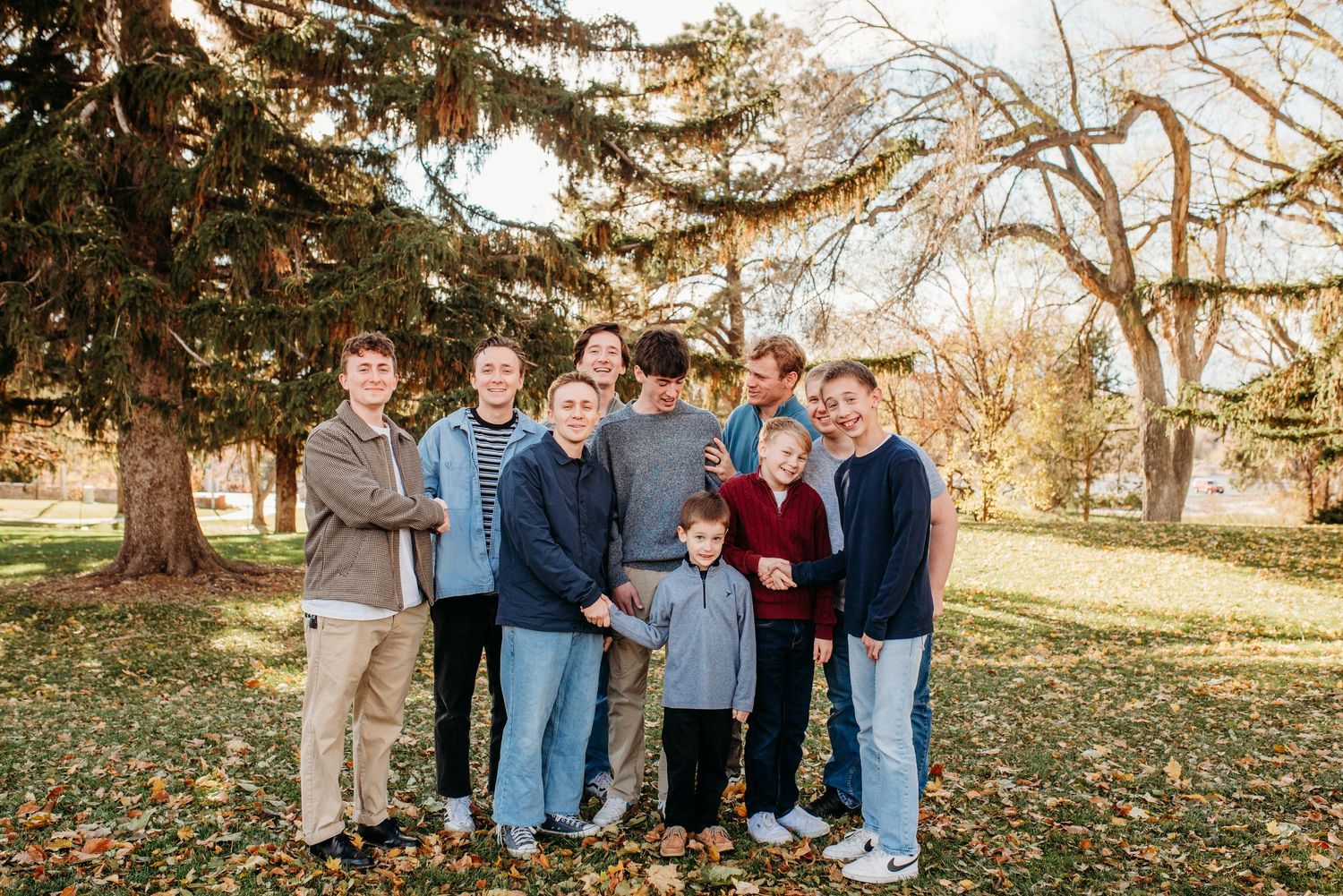 Group portrait of people gathered together under evergreen trees in fall park.