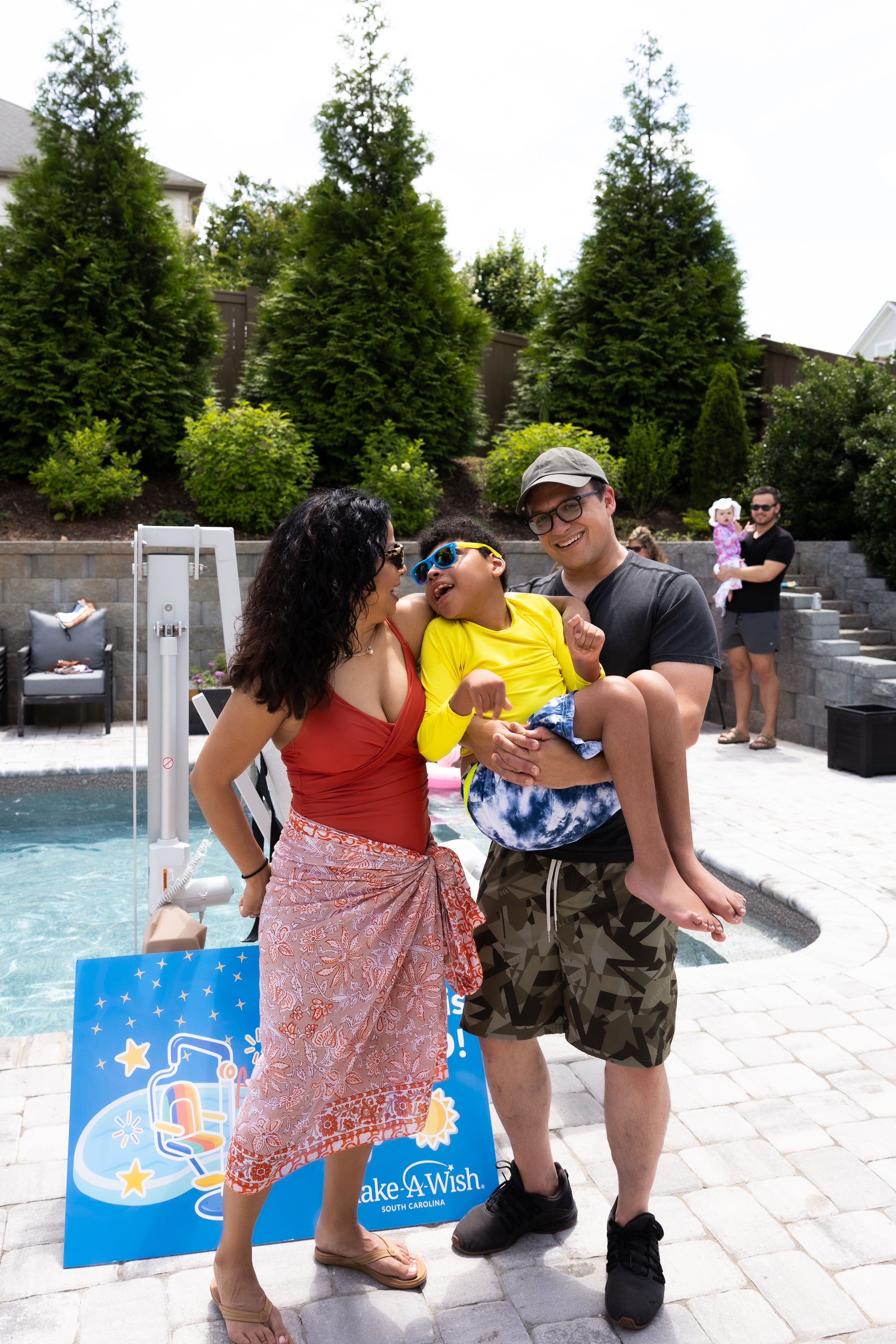 Group gathering by a swimming pool with Make-A-Wish Foundation sign and summer decorations. Greenville SC Event Photographer